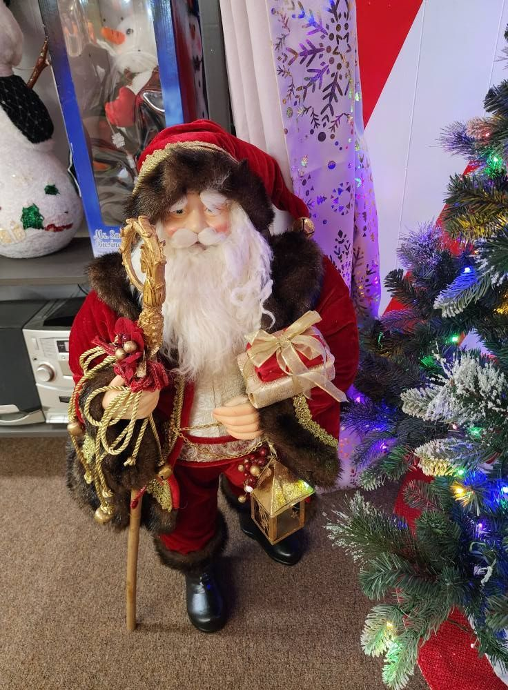 Santa Claus figure with gifts and staff, near a decorated Christmas tree.