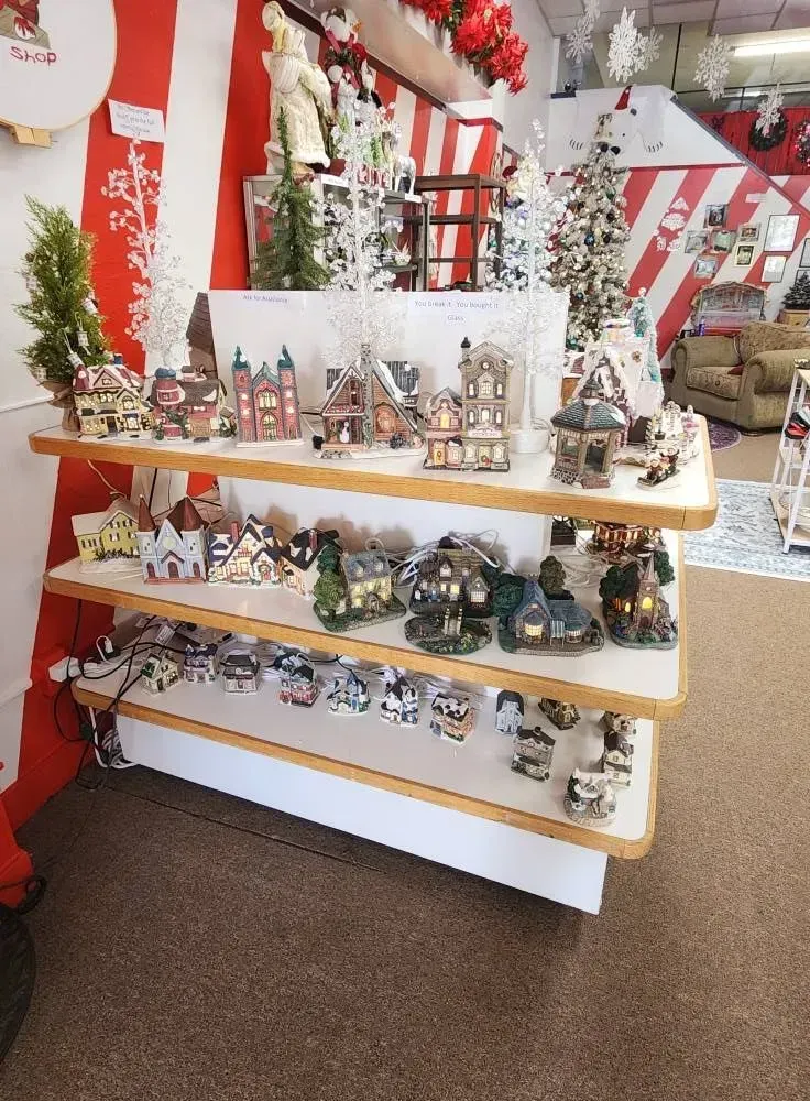 Christmas village display on a three-tiered shelf in a retail store with red and white striped background.