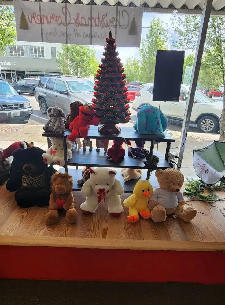 Shop window display with teddy bears and a Christmas tree; cars and buildings in the background.