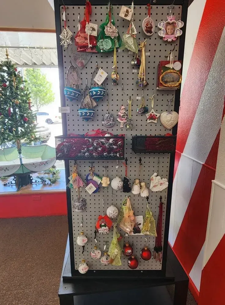 Display of Christmas ornaments on a gray pegboard in a store. Red and green decorations are visible.
