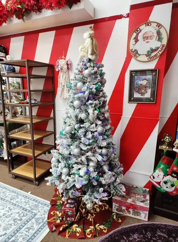 Christmas tree decorated with ornaments, in front of red and white striped wall, surrounded by gifts and decorations.