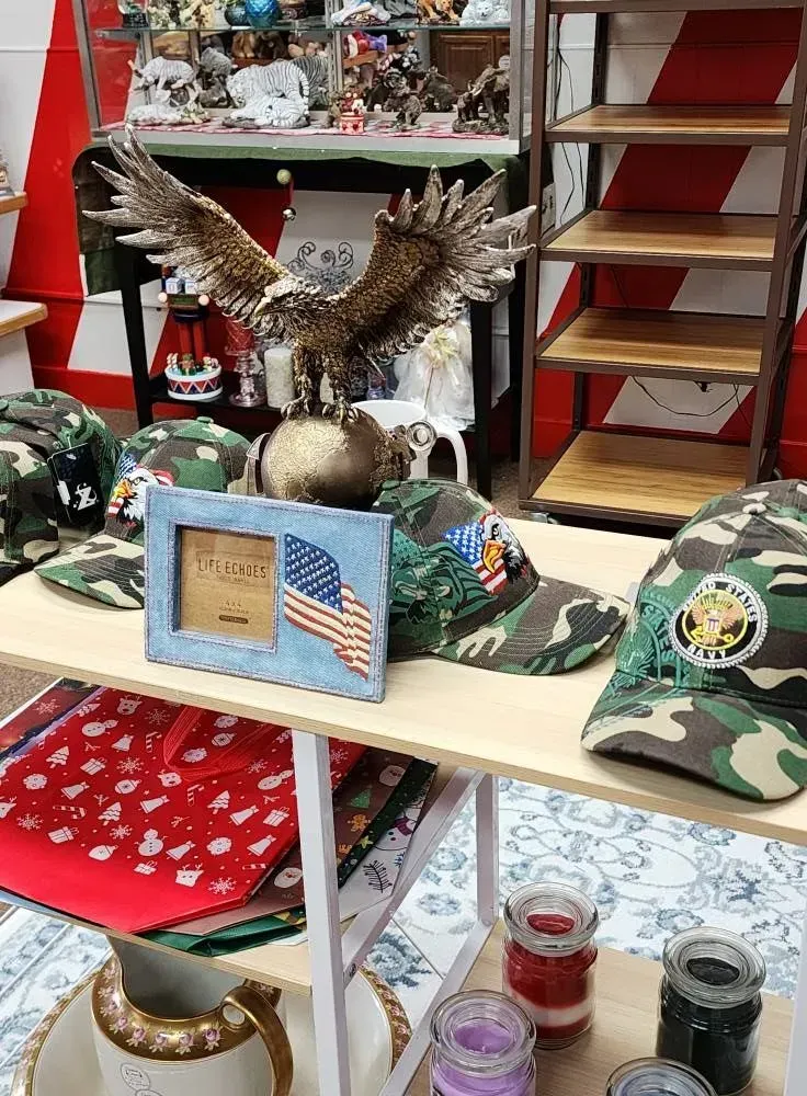 Display table with eagle statue, camo hats, American flag frame, candles, and shelf display with decor.