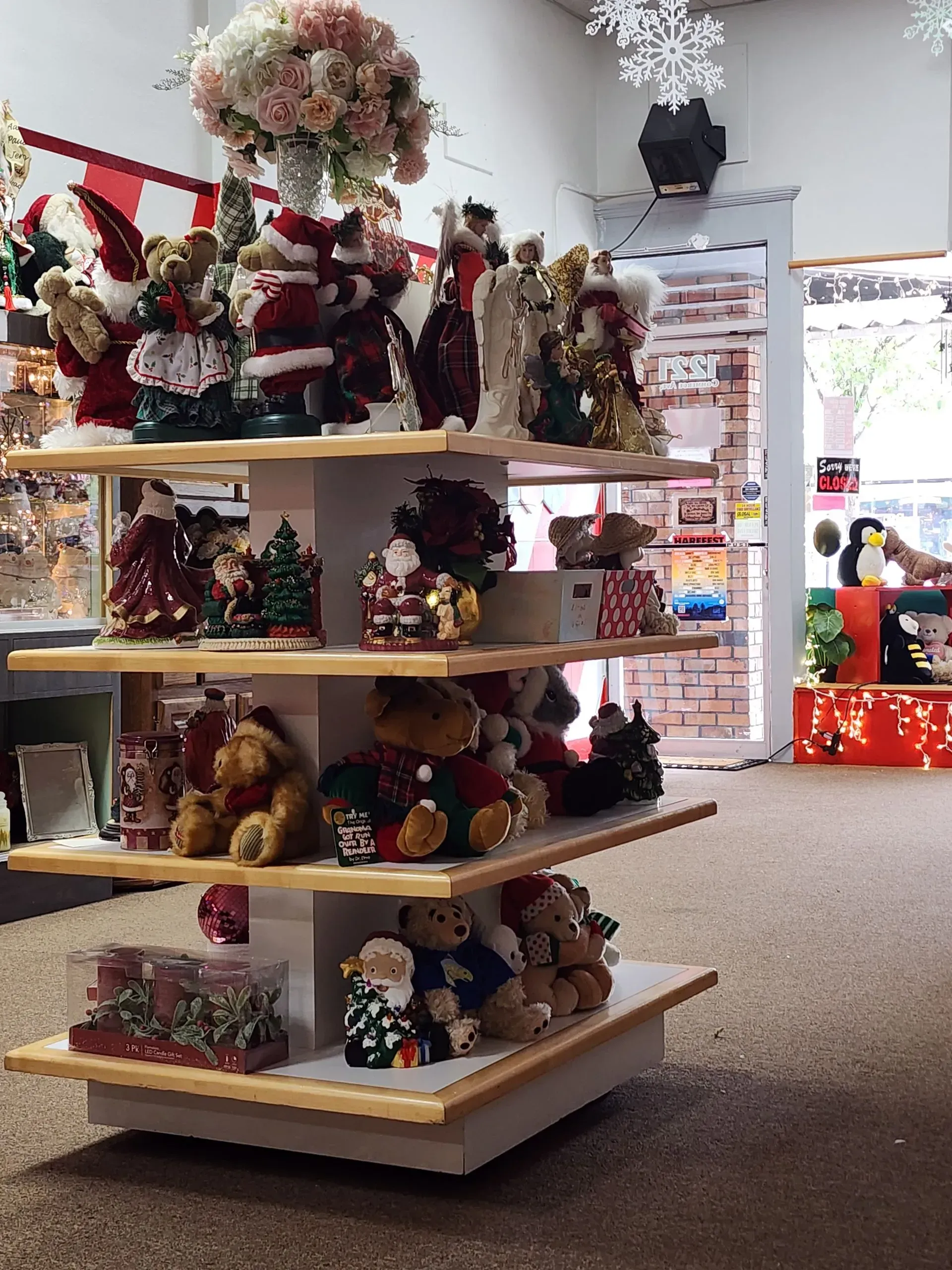 Shelves displaying Christmas decorations in a store: bears, Santas, angels, and floral arrangements.