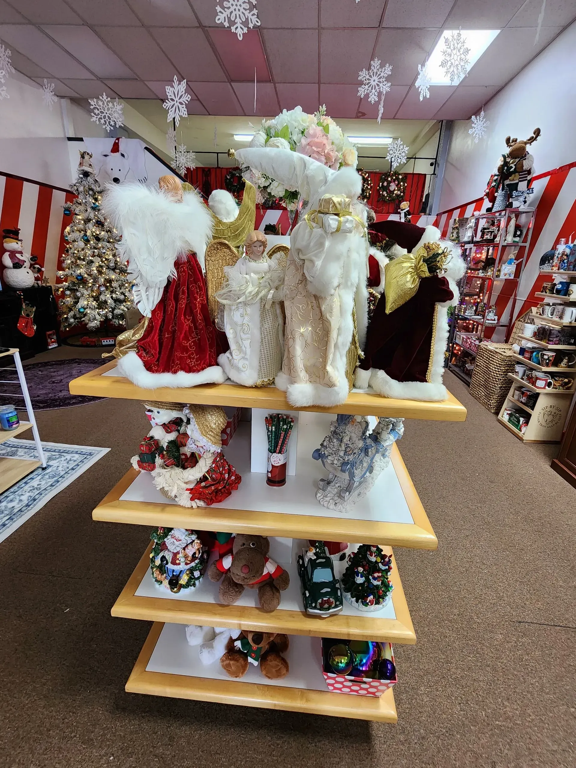 Christmas decorations on display in a store, including Santas, angels, and ornaments on tiered shelves.