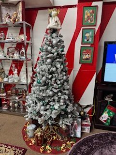Flocked Christmas tree with ornaments, angel topper, and presents. Set against red and white striped wall.
