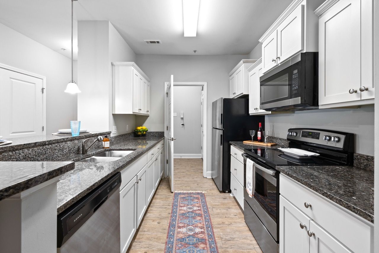 Galley-style kitchen in a modern apartment with white cabinets, granite countertops, and stainless-steel appliances at The Enclave Apartments.