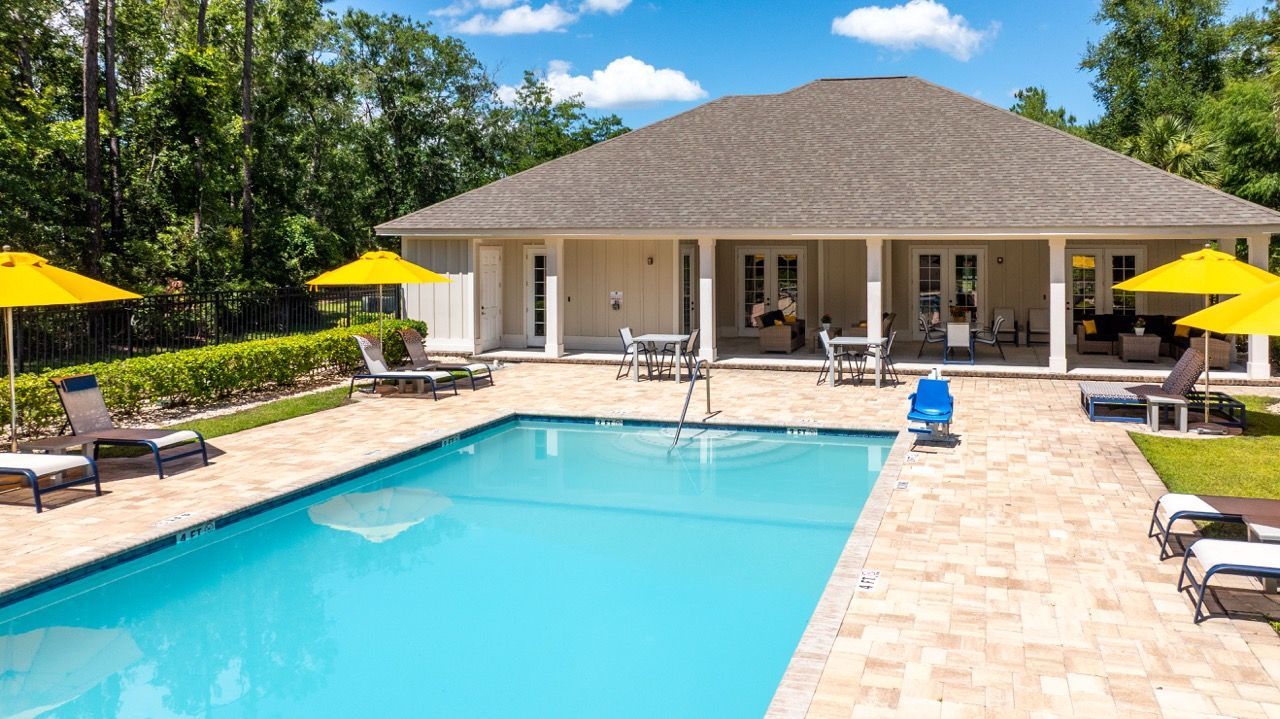 Outdoor pool area with lounge chairs, yellow umbrellas, and a clubhouse building at The Enclave Apartments.