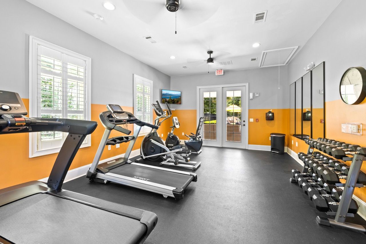 Interior view of a community gym: treadmills, stationary bikes, dumbbells, and mirrors at The Enclave Apartments.