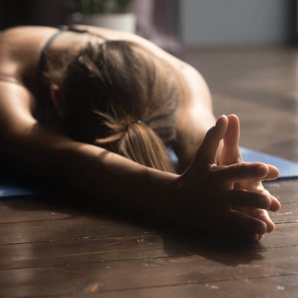 A person in a yoga pose, lying face down on a mat with arms extended forward and hands clasped together.
