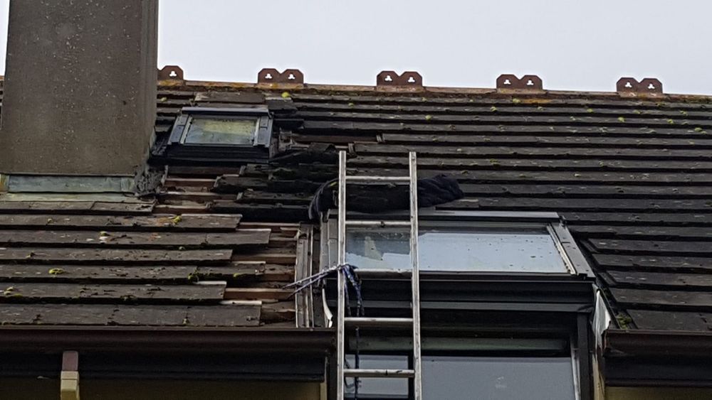 Roof under construction with blue underlayment, wooden beams, and stacked dark tiles.