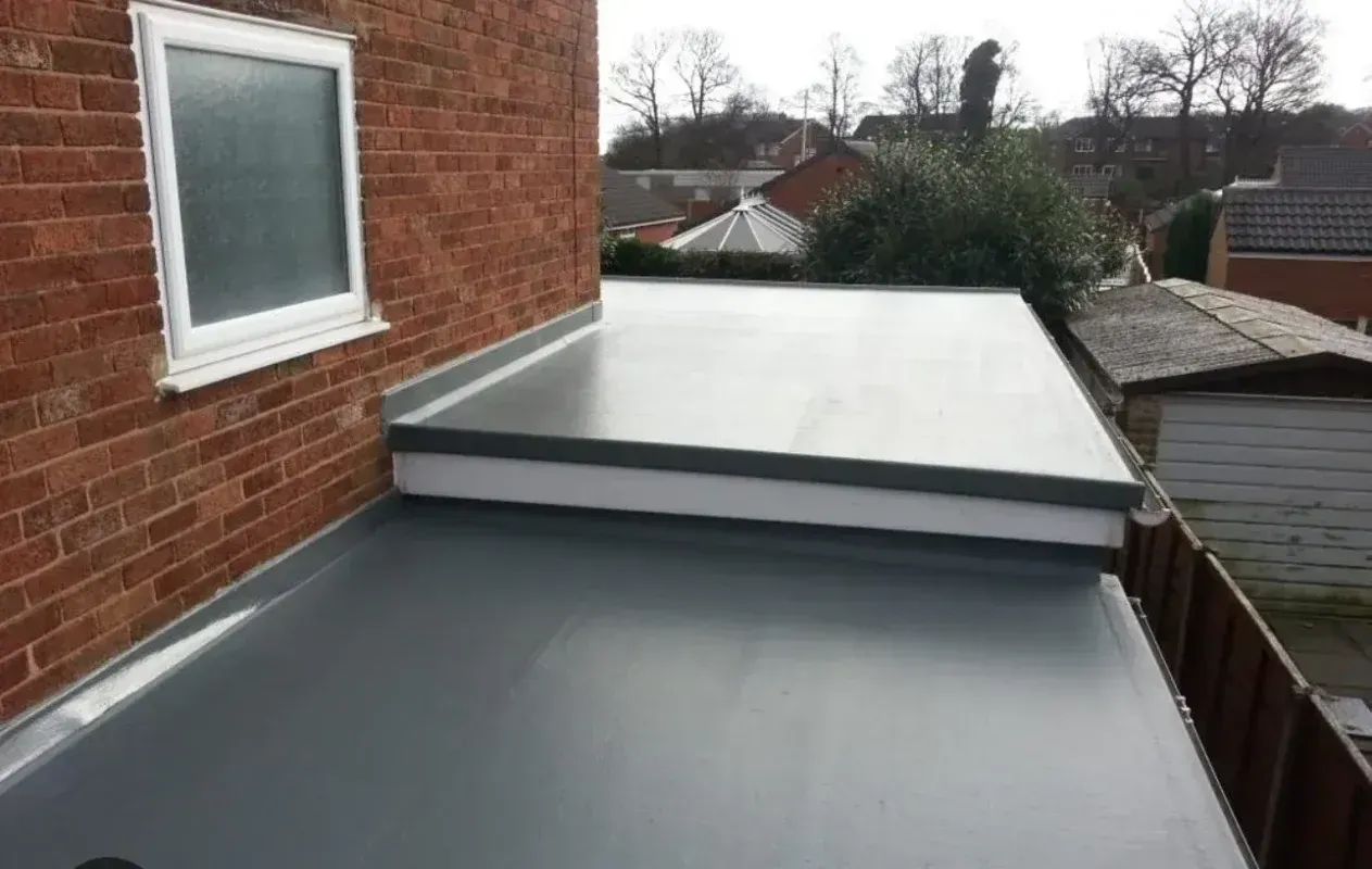 Flat, grey roof next to a brick wall with a white-framed window.
