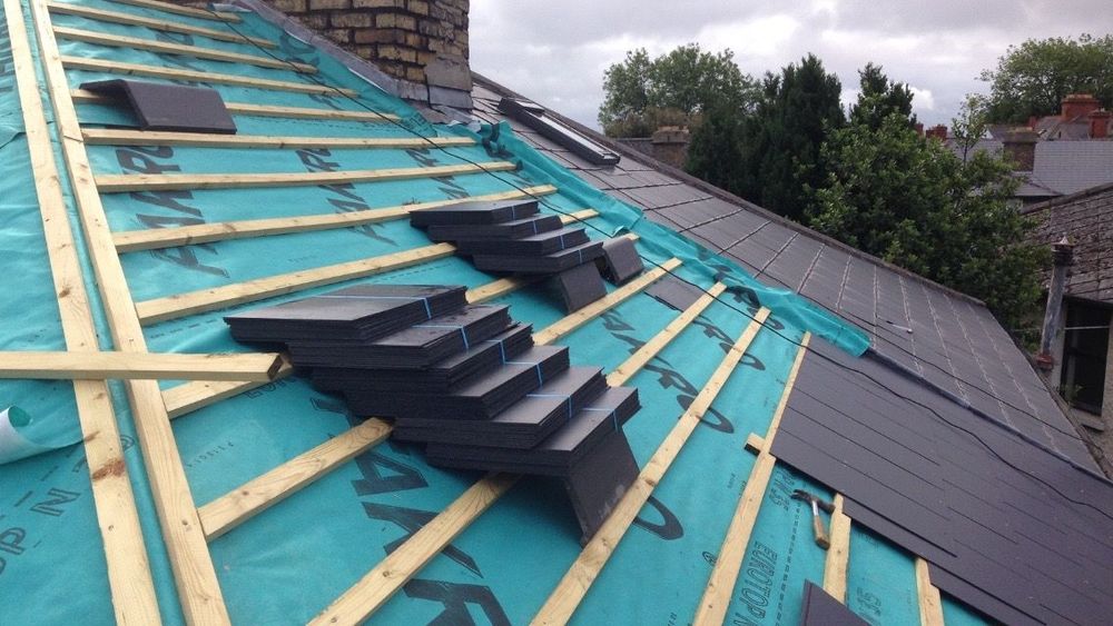 Slate roof with dormer window, metal trim, and decorative railing against a cloudy sky.