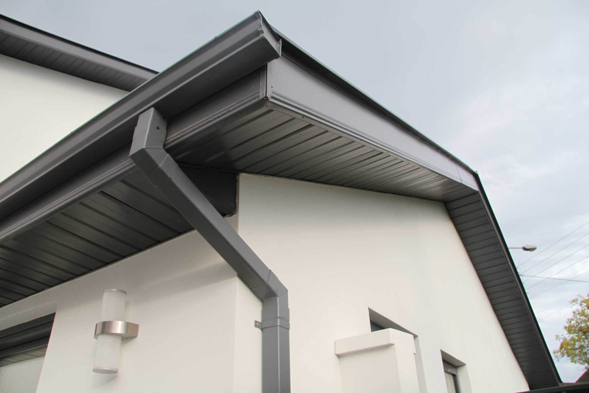 Gray gutters and soffit on a white building against a cloudy sky.