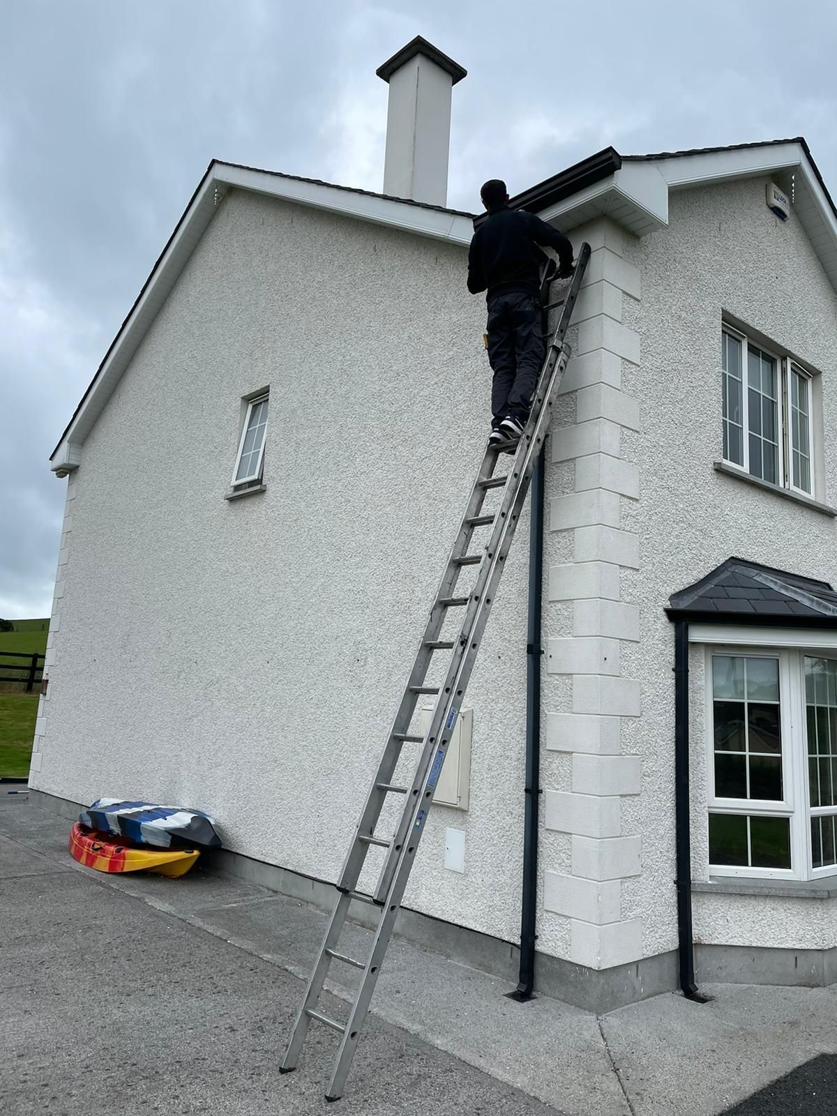 Two workers installing soffit on a brick house under a blue sky. One on a ladder, the other using a drill.