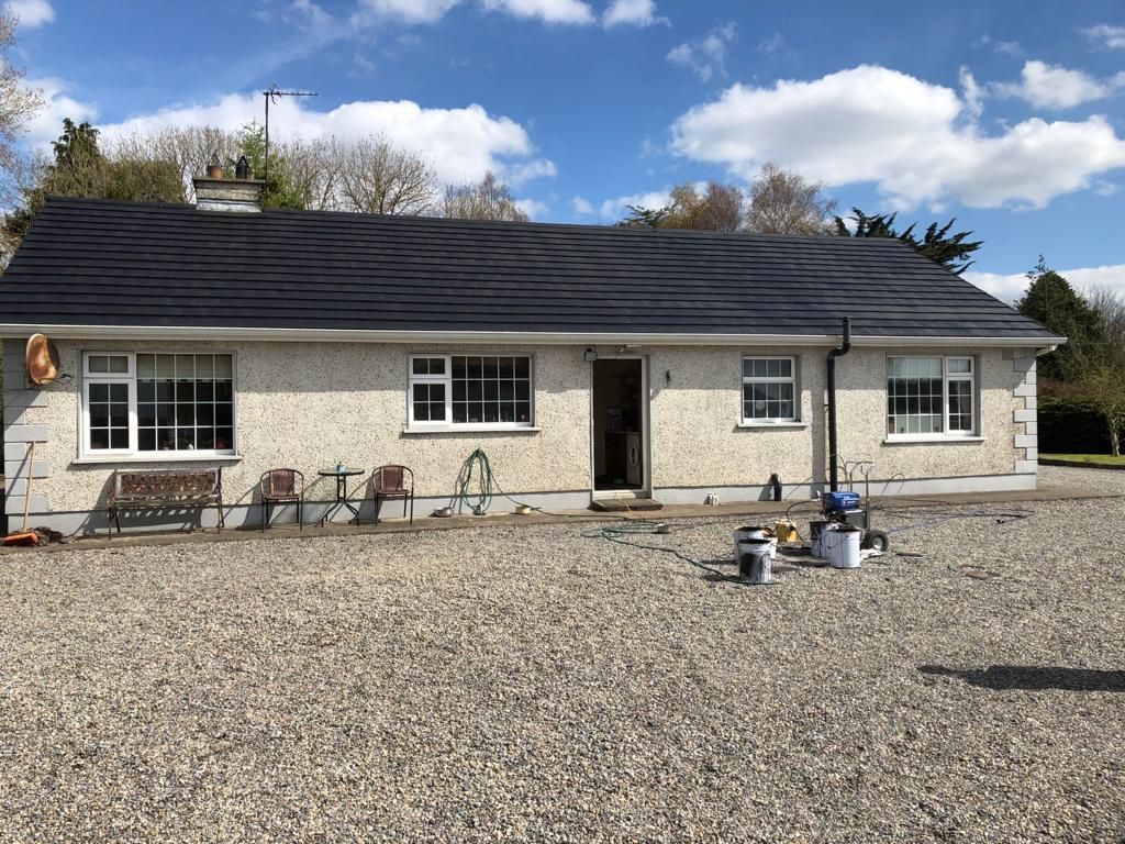 Slate roof with dormer window, metal trim, and decorative railing against a cloudy sky.