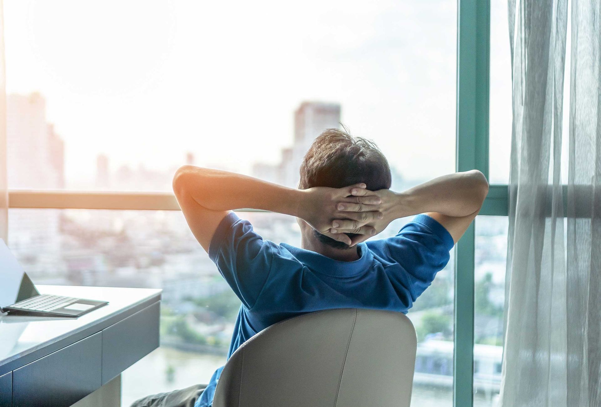 Person reclining in a chair with hands behind head, looking out a bright office window. Person reclining in a chair with hands behind head, looking out a bright office window.