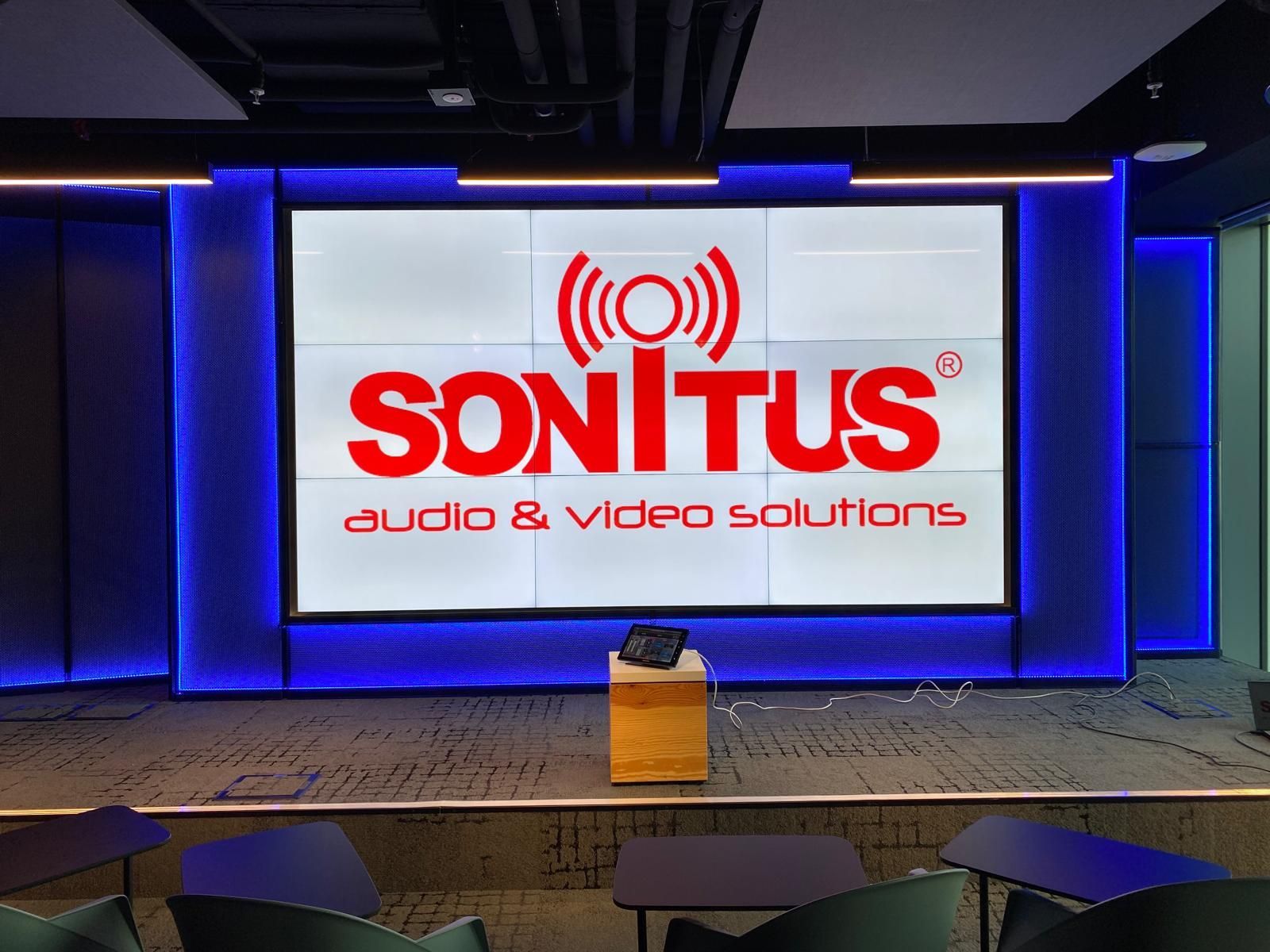 Manifesto promozionale per le soluzioni audio e video Sonitus in un grande teatro, con altoparlanti e grafica a onde rosse.