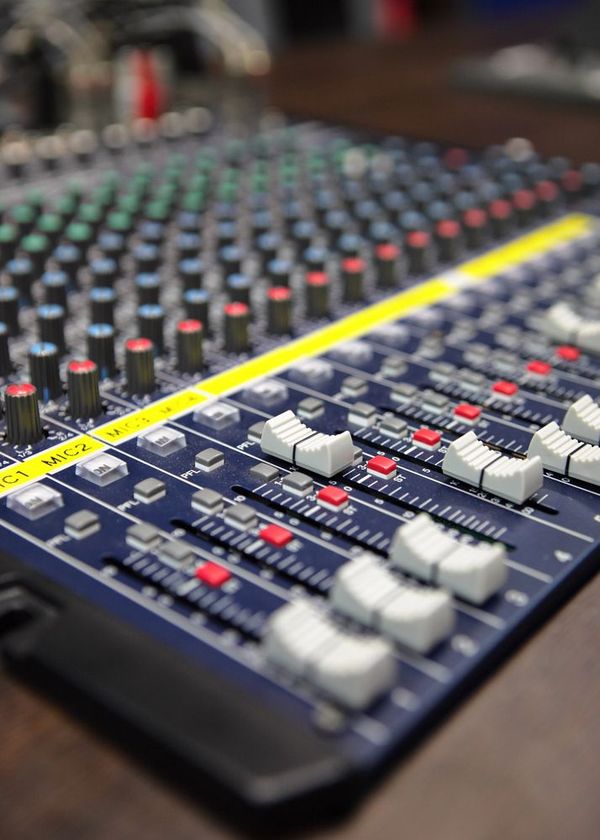 Console di mixaggio audio con manopole, fader e pulsanti, in blu scuro e dettagli colorati.