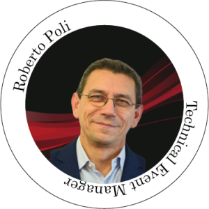 Roberto Poli, responsabile tecnico dell'evento, sorridente, con gli occhiali, davanti a uno sfondo rosso e nero.