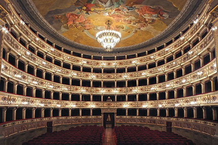 Vista interna di un teatro decorato a più livelli, con posti a sedere rossi e un soffitto a cupola dipinto.