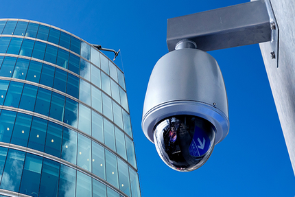 Telecamera di sicurezza montata all'esterno di un moderno edificio in vetro; sfondo cielo azzurro.