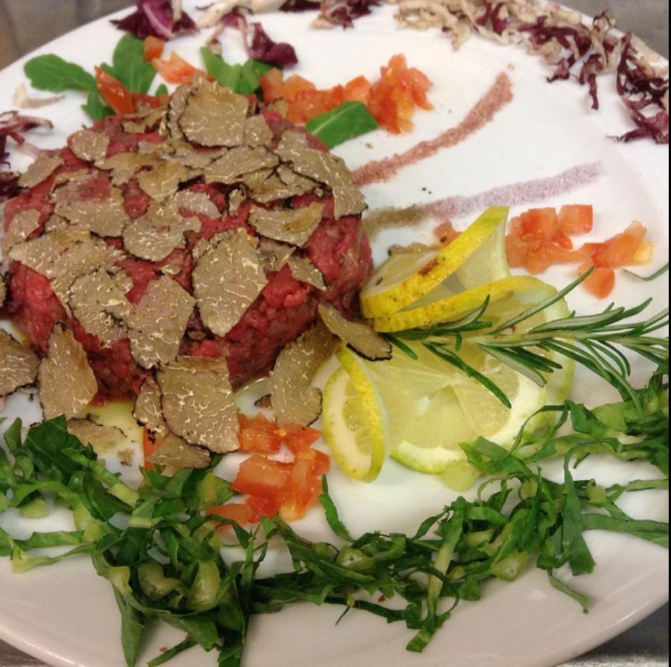 Un piatto bianco con sopra carne, verdure e fette di limone