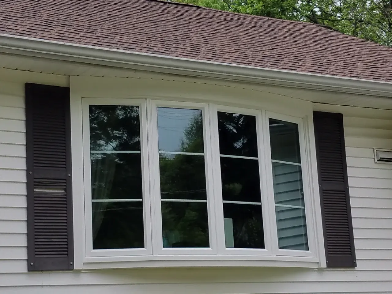White bay window with dark shutters on a house exterior under a shingled roof
