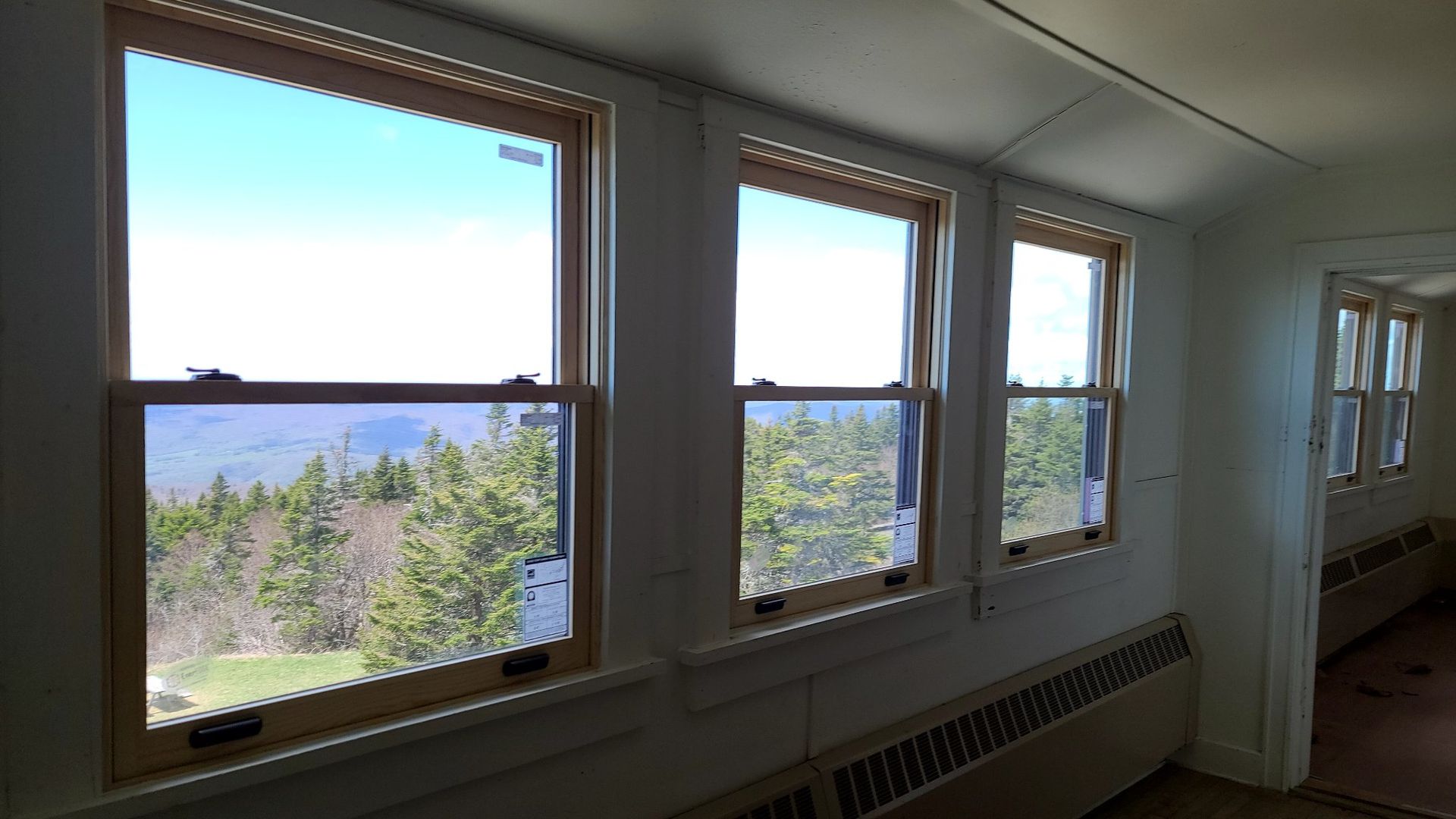 Sunlit room with three windows overlooking trees and mountains, and a radiator beneath the windows.