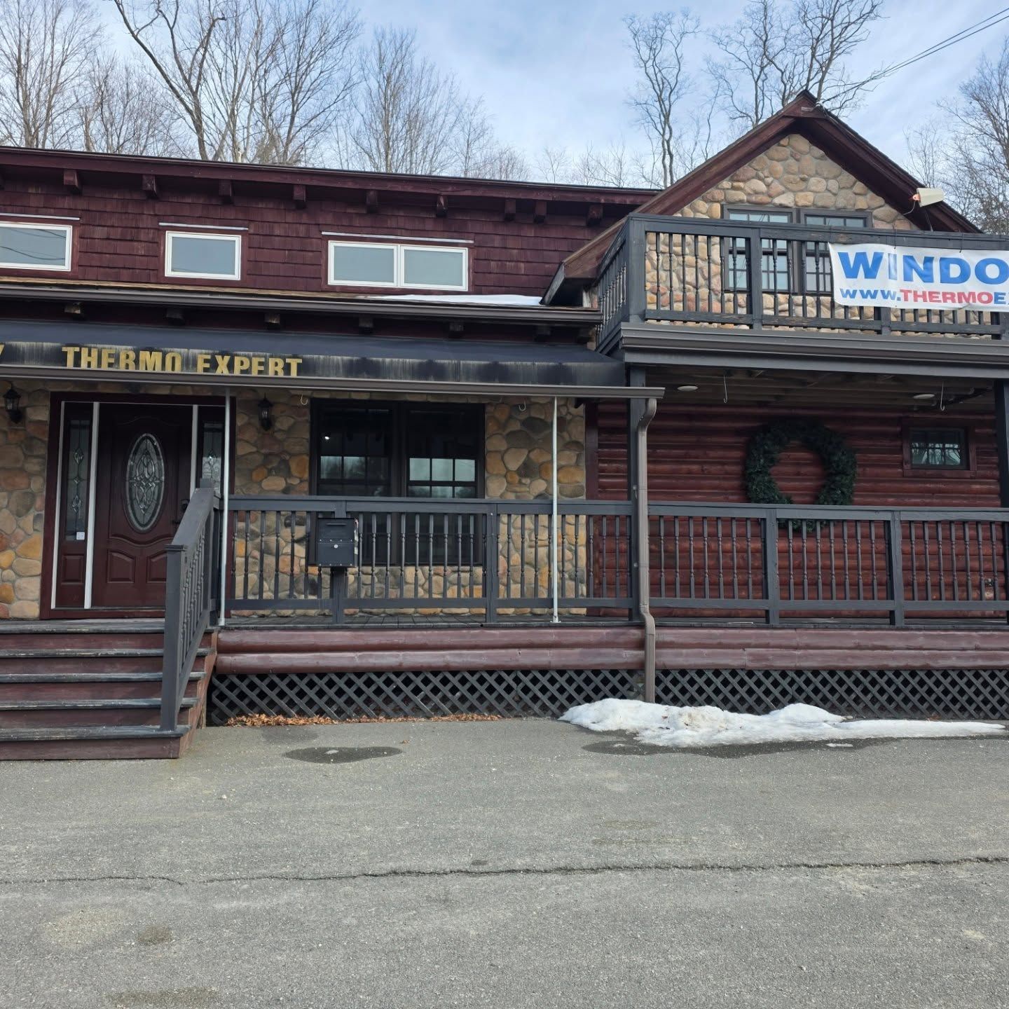 Log cabin storefront with porch railing and signs for The Thermo Expert and WNDO Windows, seen from the street