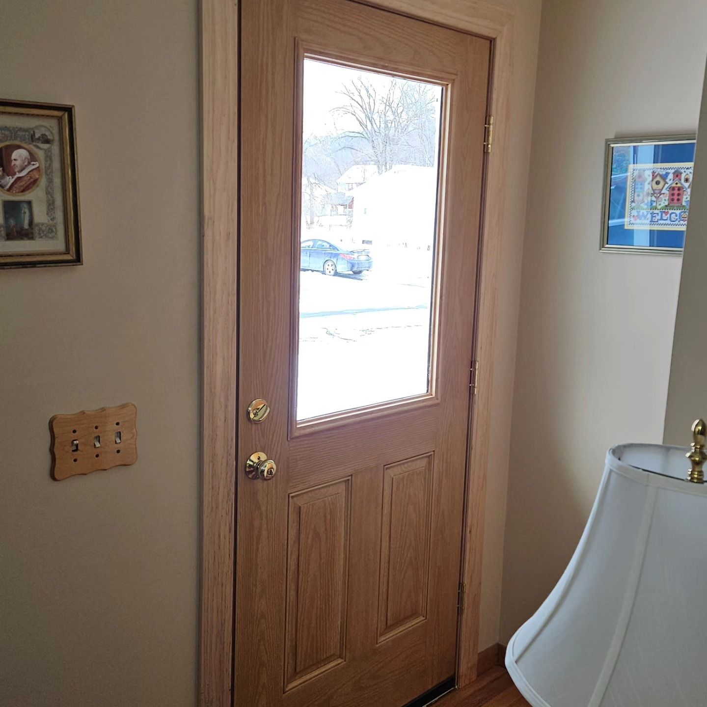 Interior view of a wooden front door with a glass panel showing a snowy yard outside