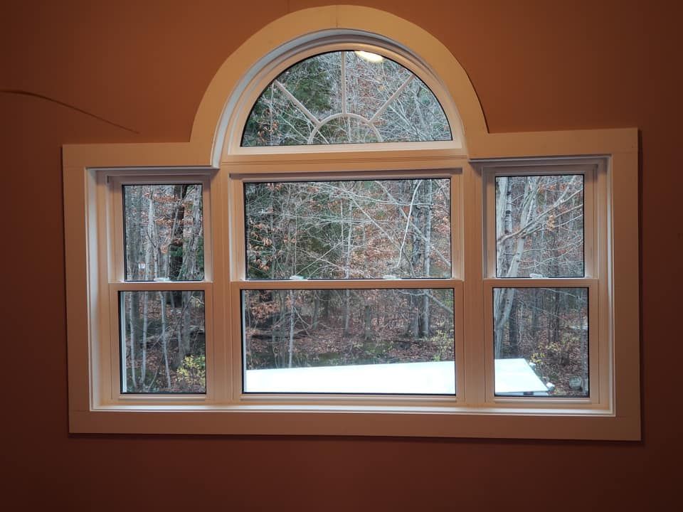 Arched window with white trim looking out onto snowy woods