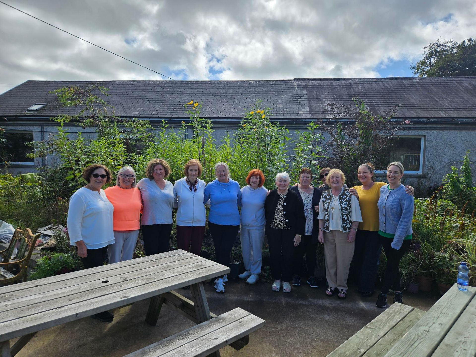 Group of people standing outdoors near a building with a picnic table.