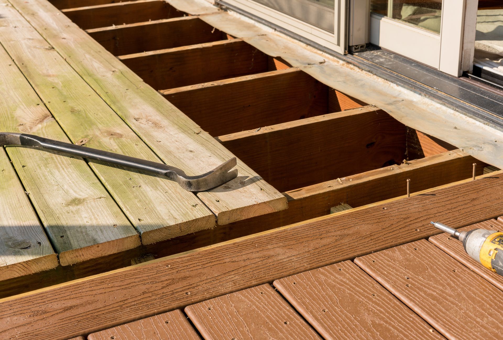 Deck repair: A pry bar rests on old wooden planks being removed, adjacent to new composite decking.