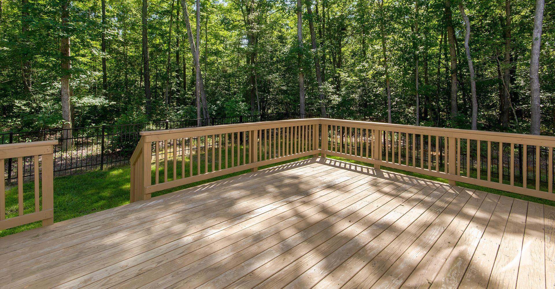 Wooden deck with railing, shaded by trees in a backyard.