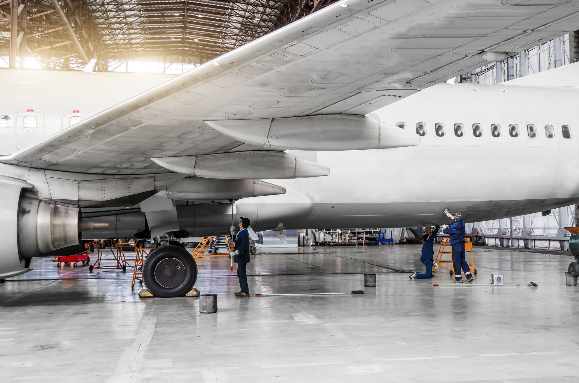 Large airplane in a hangar with workers inspecting landing gear on the polished floor. Large airplane in a hangar with workers inspecting landing gear on the polished floor.