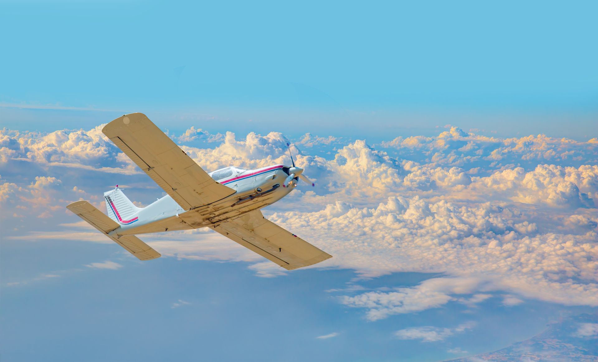 Small white propeller plane flying above golden clouds in a blue sky