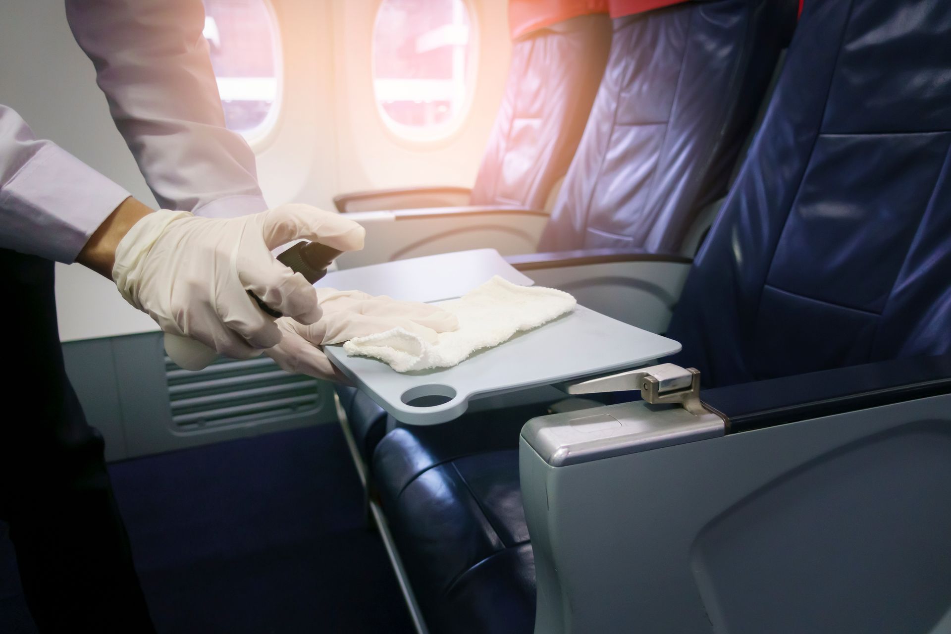 Gloved hands preparing a folded towel on an airplane tray table beside a leather seat