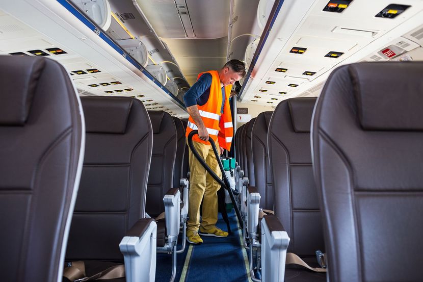 Worker vacuuming airplane cabin aisle while wearing an orange safety vest Worker vacuuming airplane cabin aisle while wearing an orange safety vest