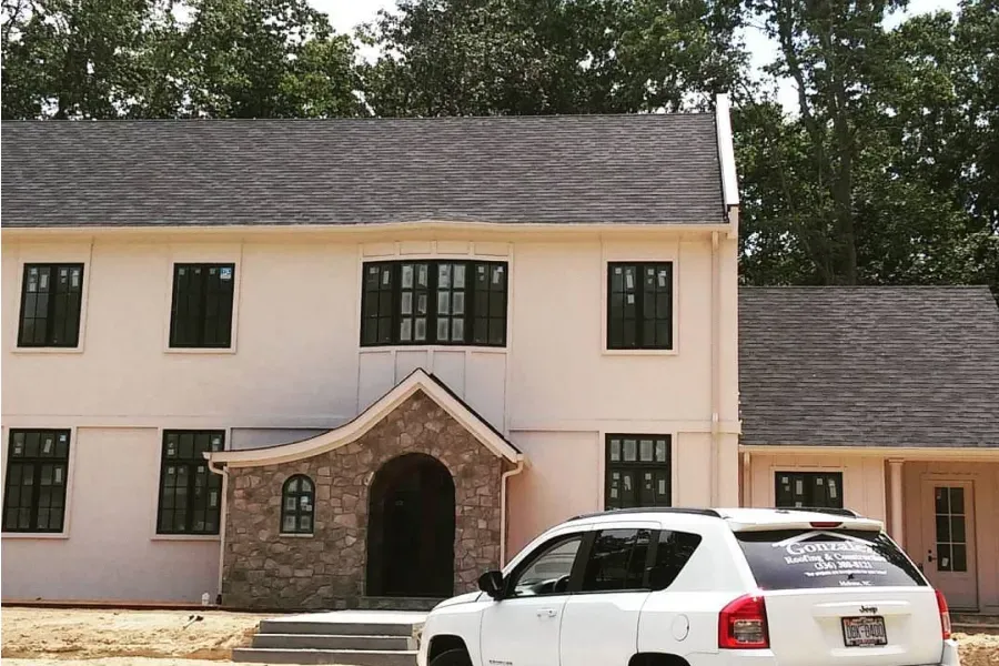 A white car is parked in front of a large house