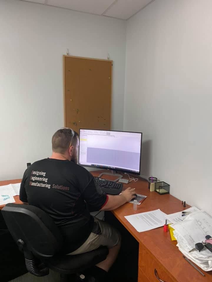 A Man Is Sitting At A Desk In Front Of A Computer — D.E.M Solutions Pty Ltd In Caboolture, QLD
