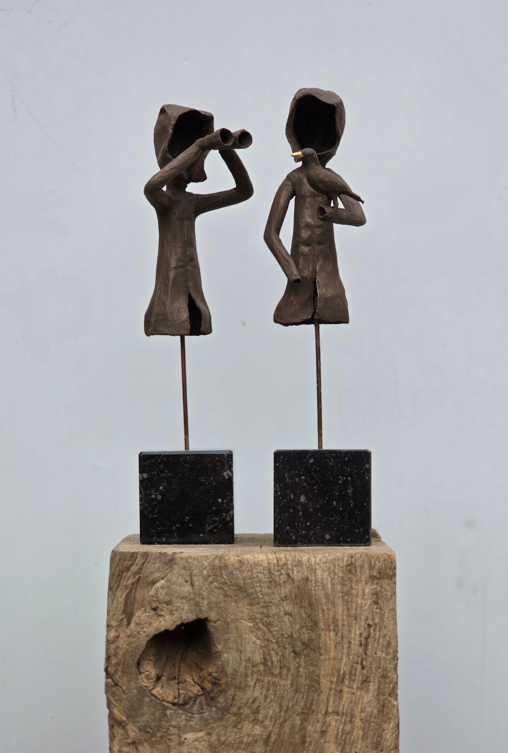 Twee sculpturen van mensen die naast elkaar op een houten blok staan.