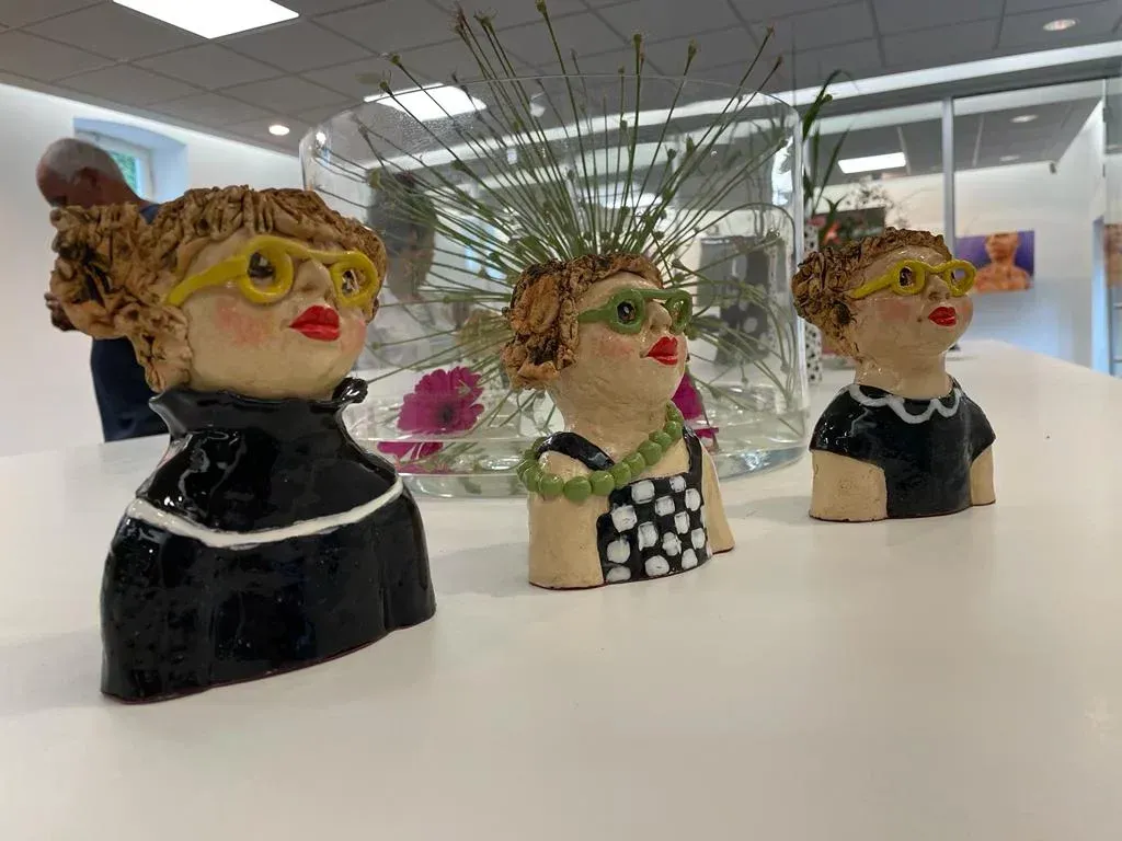 Op een tafel staan ​​drie keramische beeldjes van vrouwen met een bril.