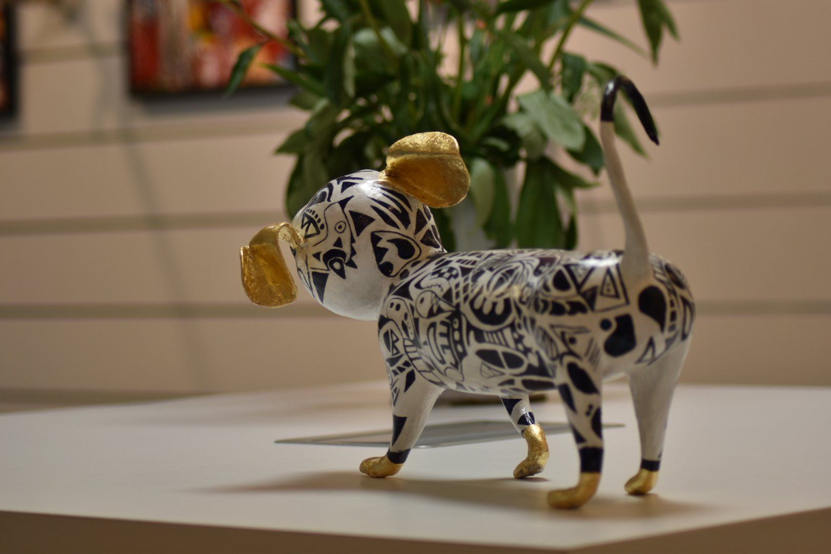 Een beeld van een hond zit op een tafel voor een plant.