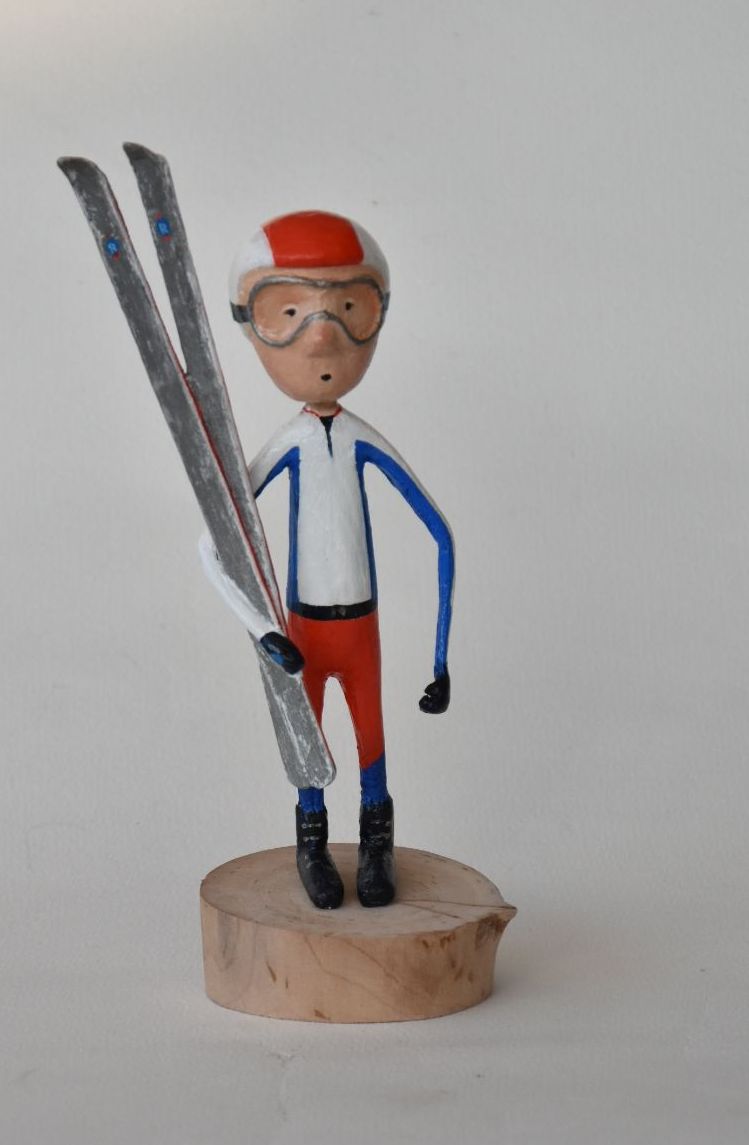 Een beeldje van een man die ski's vasthoudt op een houten voetstuk