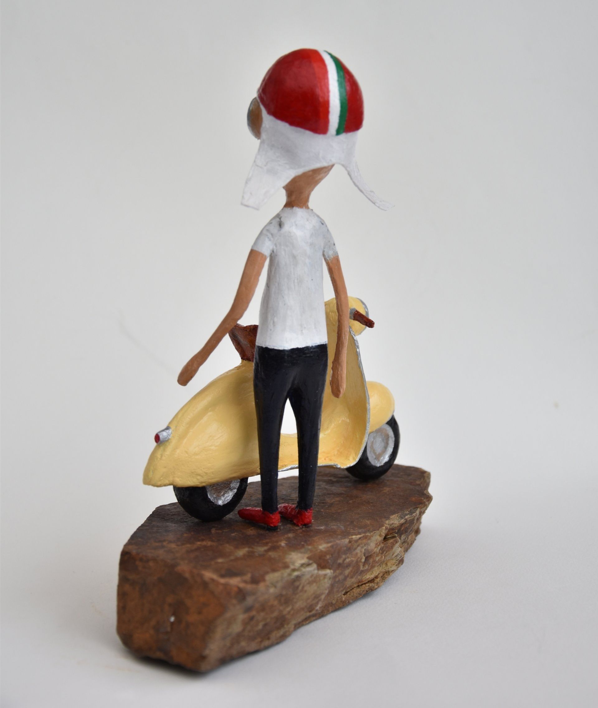 Een standbeeld van een man met een helm die naast een scooter staat