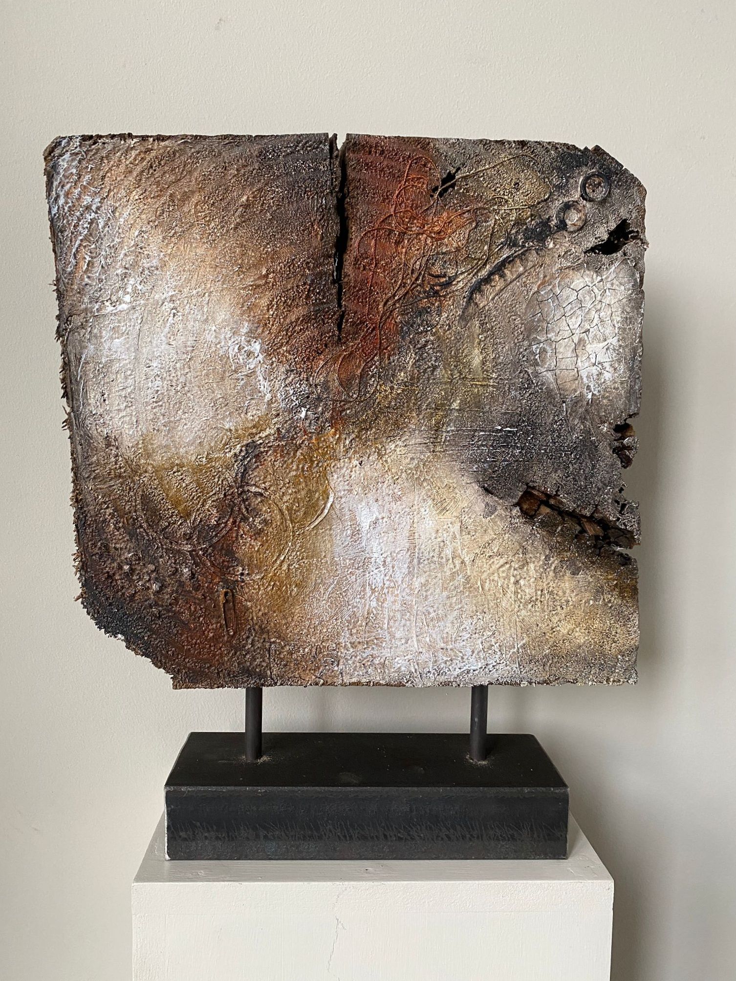 Een sculptuur van een stuk hout staat op een sokkel.