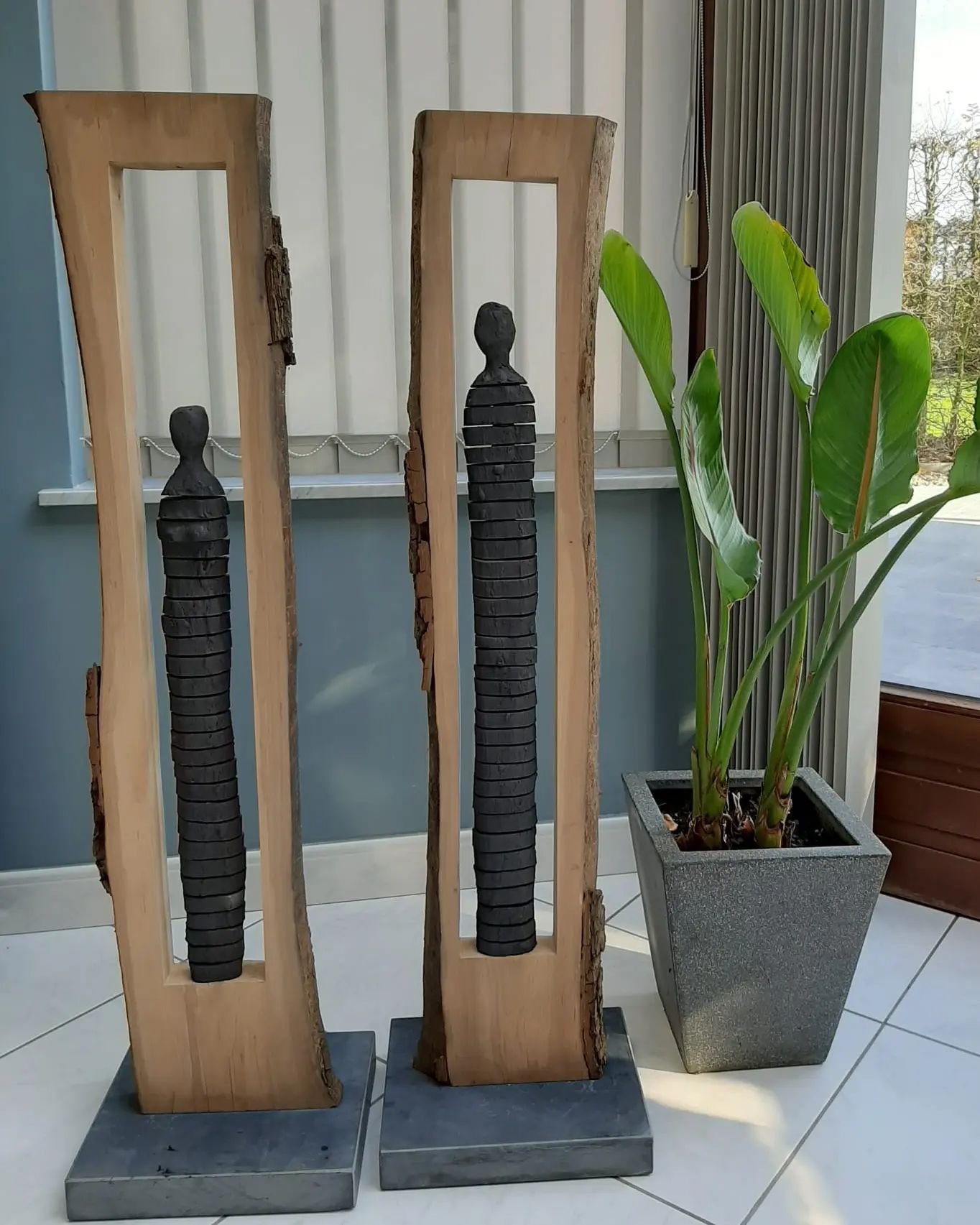 Drie houten sculpturen staan ​​naast een potplant