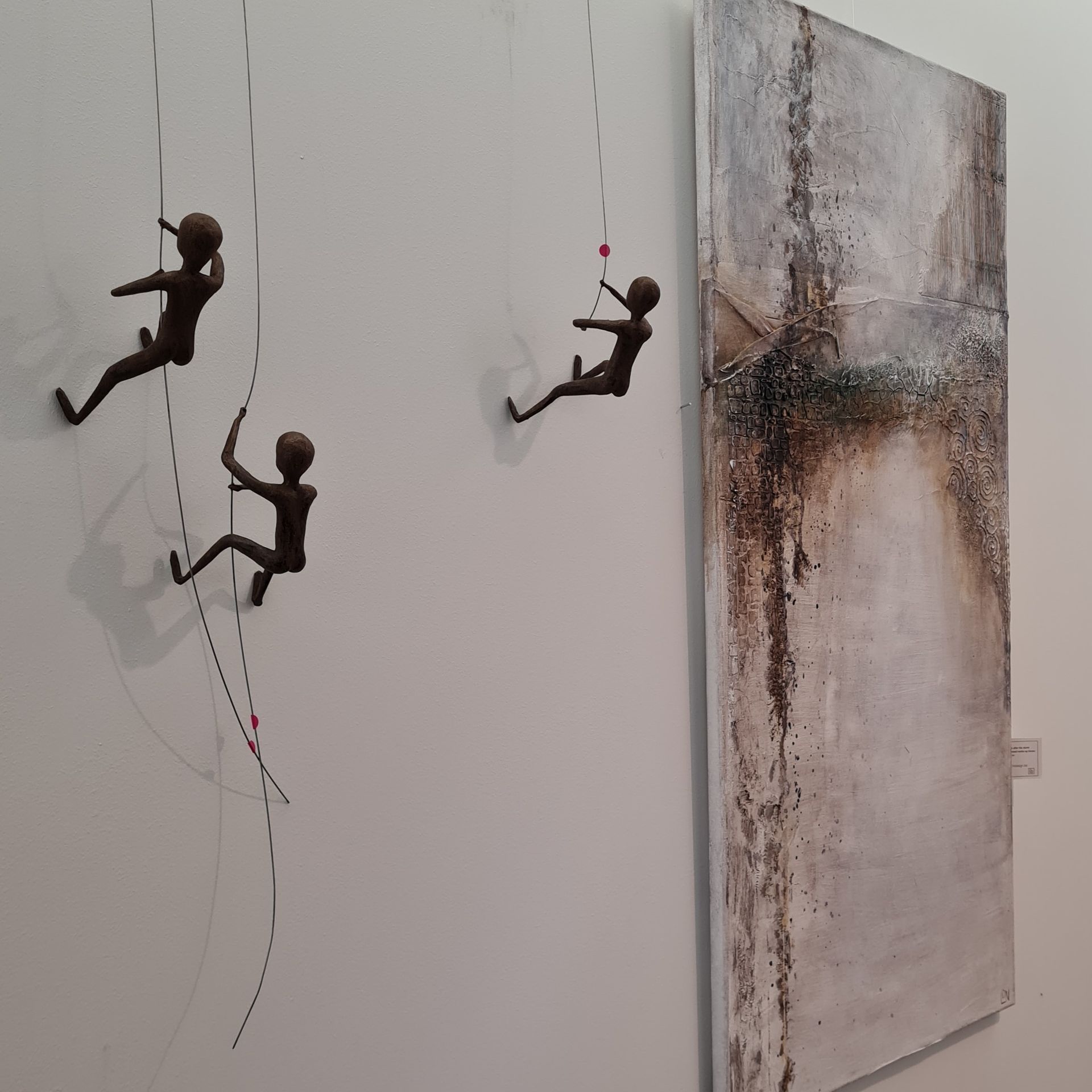 Drie sculpturen van mensen die in touwen klimmen naast een groot schilderij
