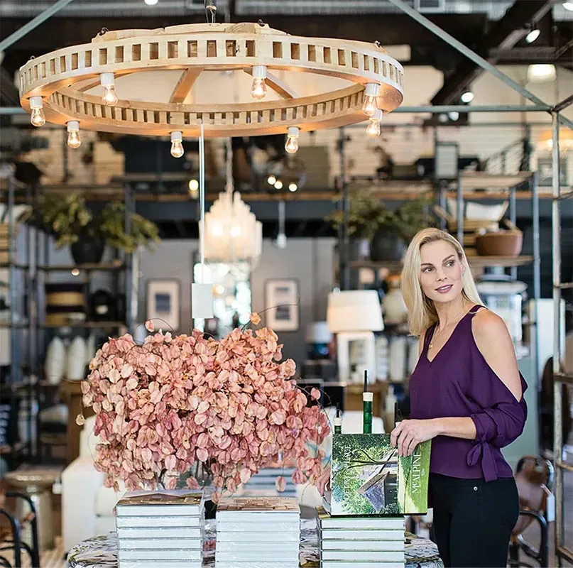 Woman in a purple top stands in a stylish boutique, holding a book.