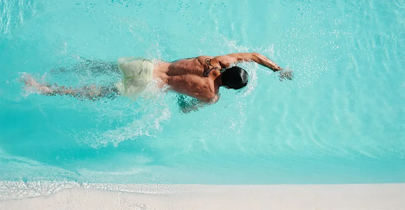 Man swimming the freestyle stroke in a bright blue pool.
